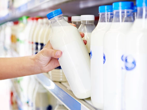 A customer chooses a bottle of milk from a well-stocked supermarket shelf