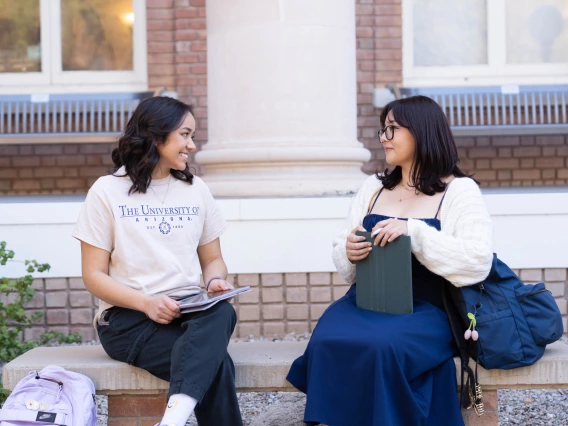 two women sittting on a bench outside having a conversation