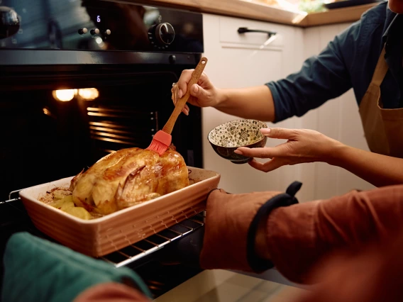 Two people open the oven to baste a turkey