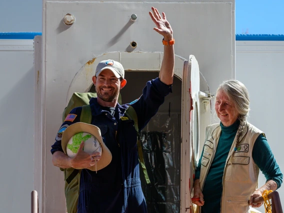 A person opens the door to a sealed habitat to as a second person exits waving and smiling.