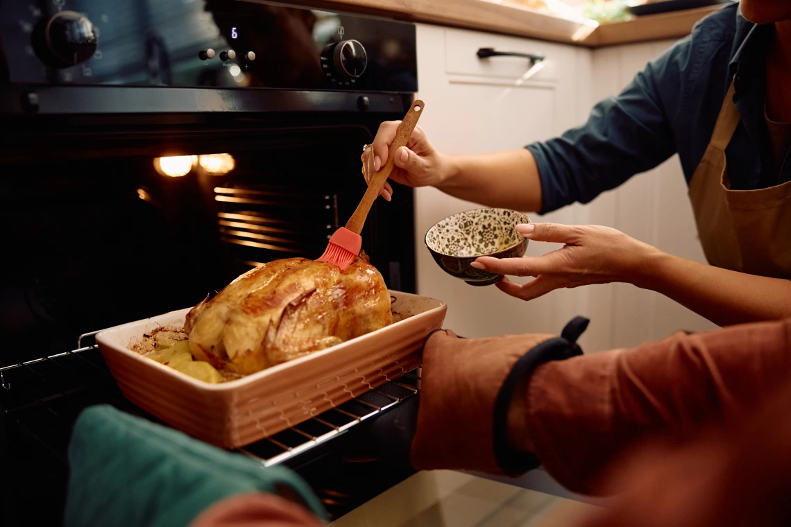 Two people open the oven to baste a turkey