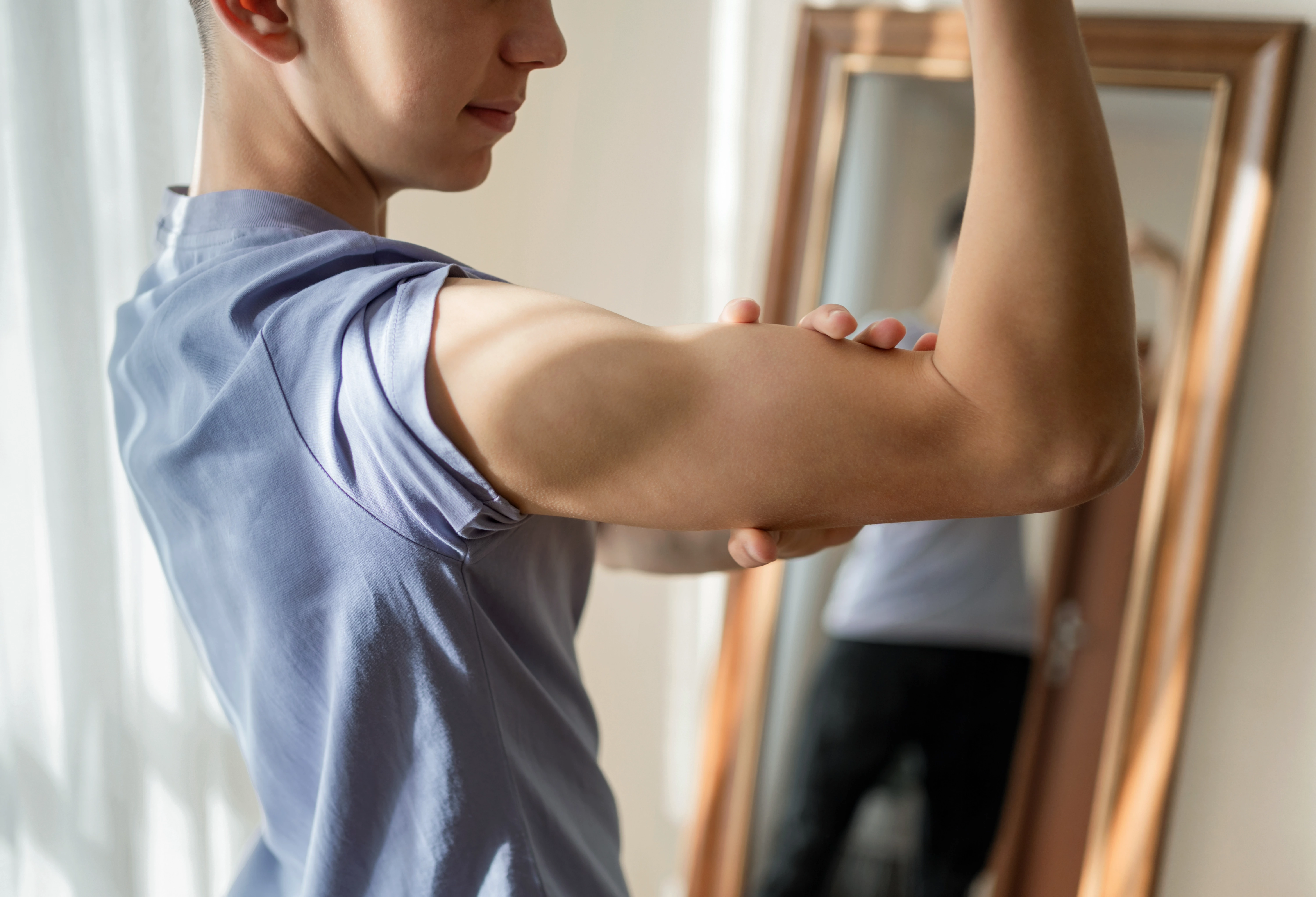 Teenage boy measures his bicep in front of a mirror